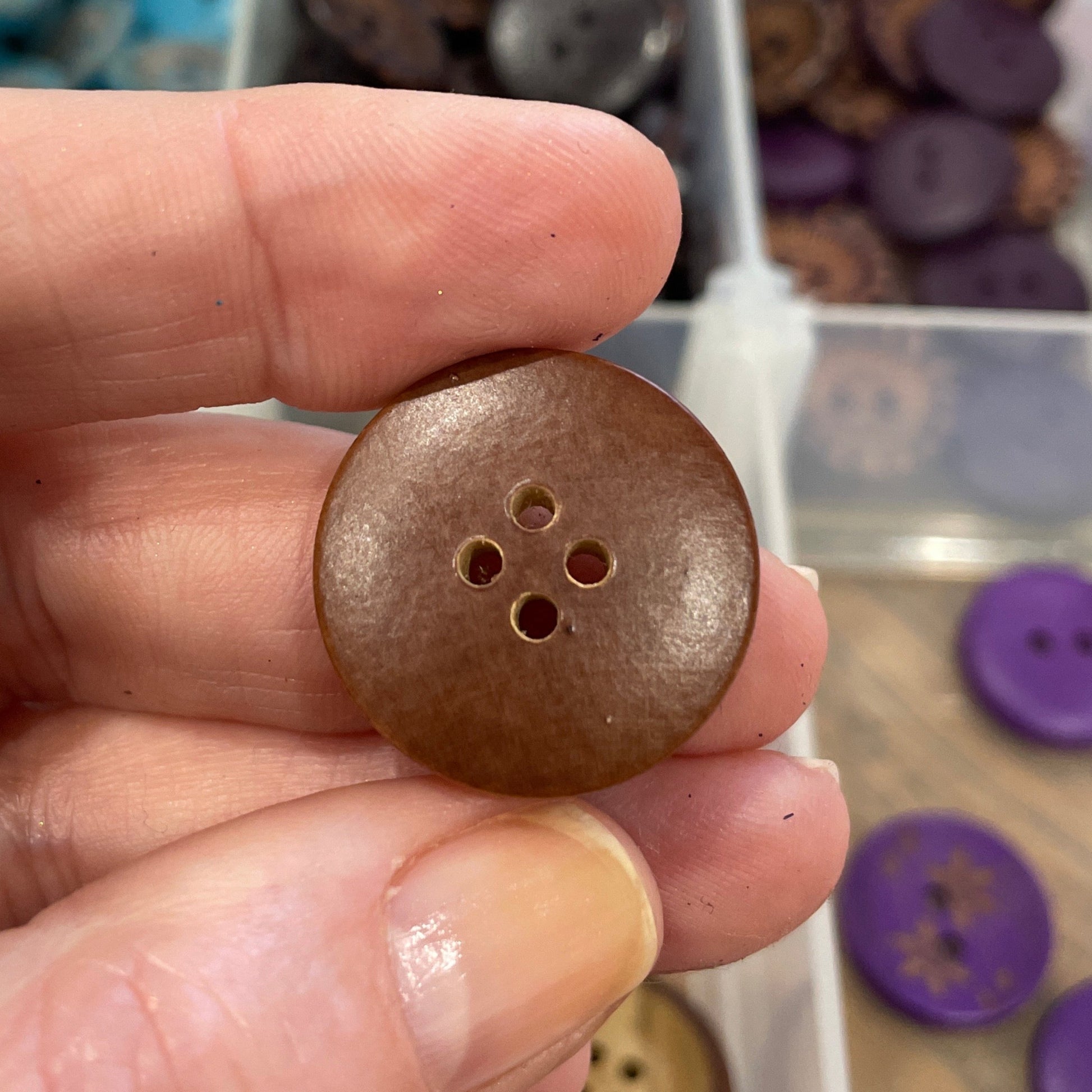 Hand holding a brown button with a clear container of buttons in the background
