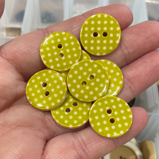 Hand holding green buttons with white polka dots in front of a container of buttons.