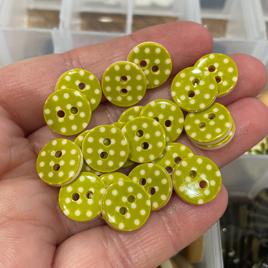 Hand holding green buttons with white polka dots in front of a container of assorted buttons.
