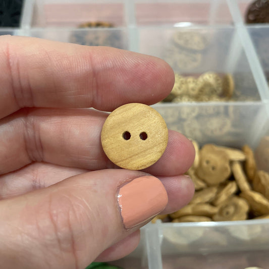 Hand holding a wooden button with a clear container of assorted buttons in the background