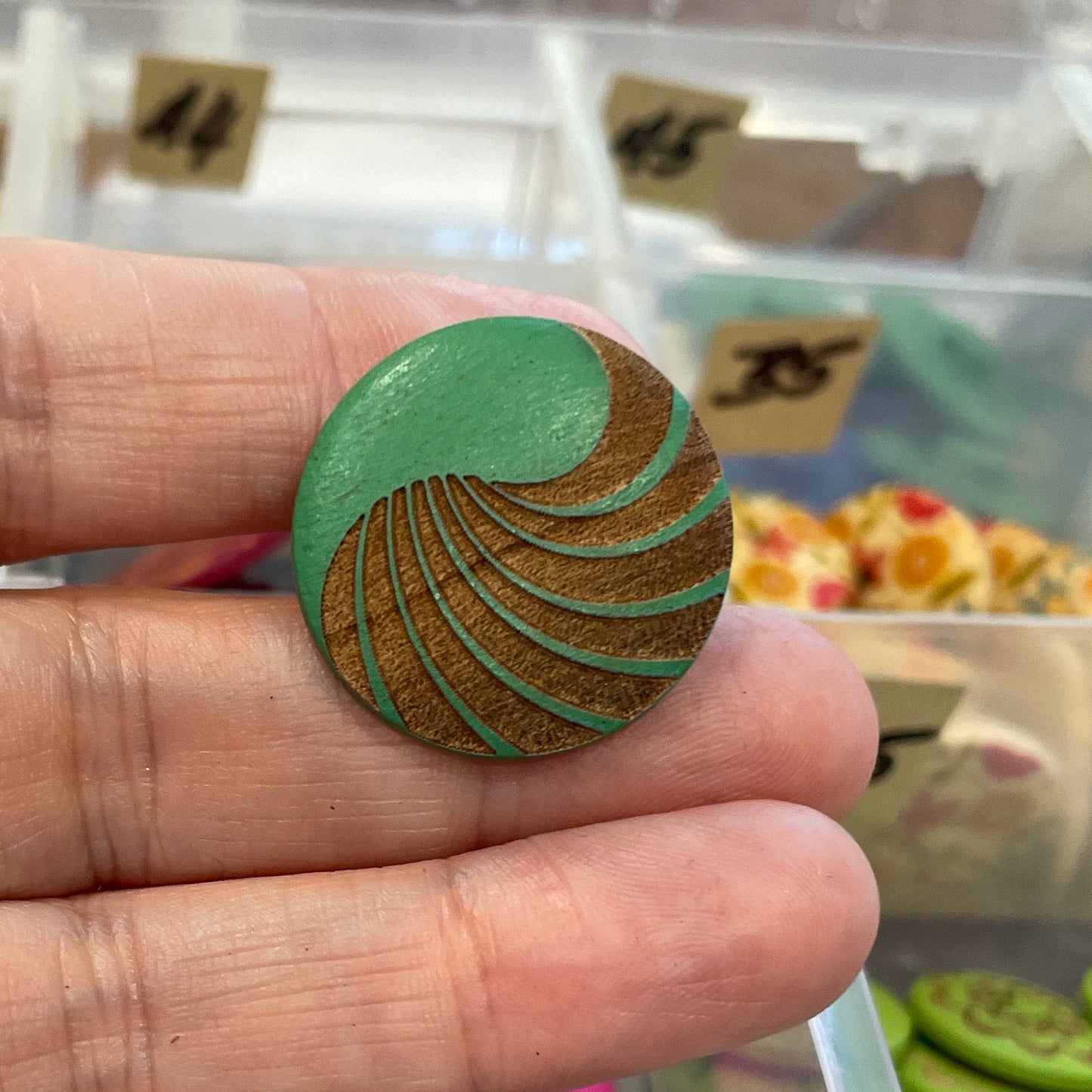 Hand holding a wooden button with a clear container of buttons in the background