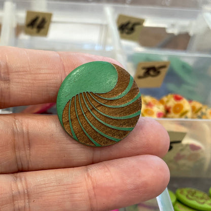 Hand holding a wooden button with a clear container of buttons in the background
