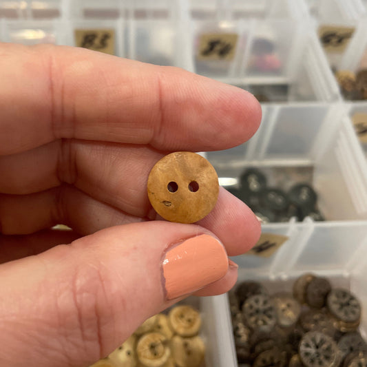 Hand holding a small gold button with a blurred background of button collection
