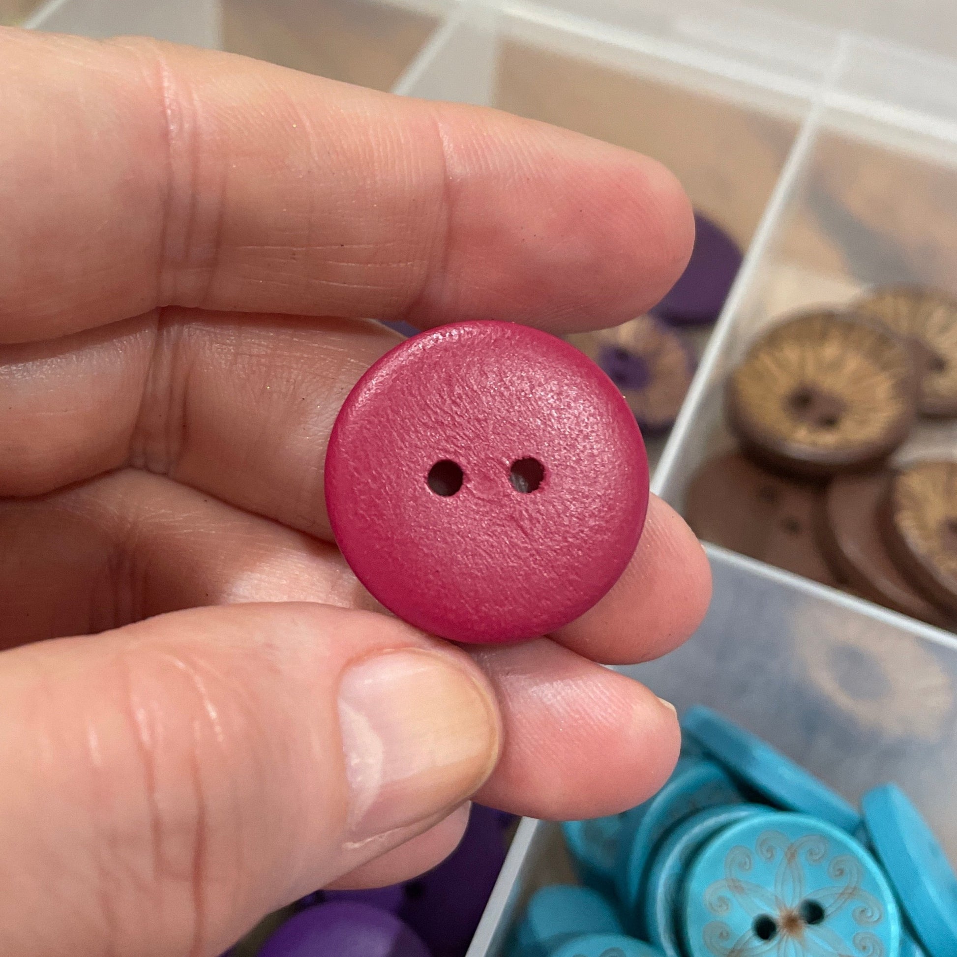 Hand holding a pink button with a container of colorful buttons in the background