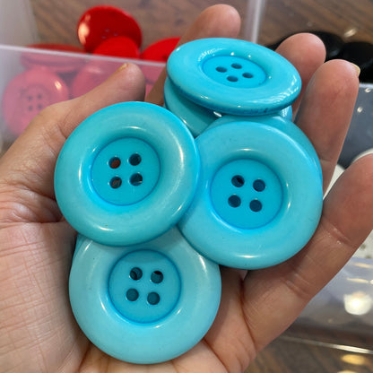 Hand holding blue buttons with a background of colorful buttons in a box.