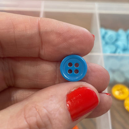 Hand holding a blue button with a clear container of buttons in the background