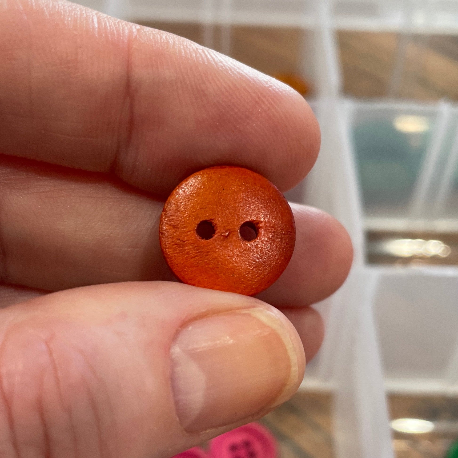 Hand holding a small orange button with a clear container of buttons in the background
