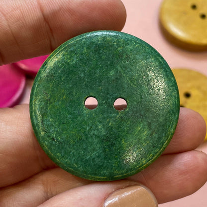 Hand holding a green button with colorful buttons in the background