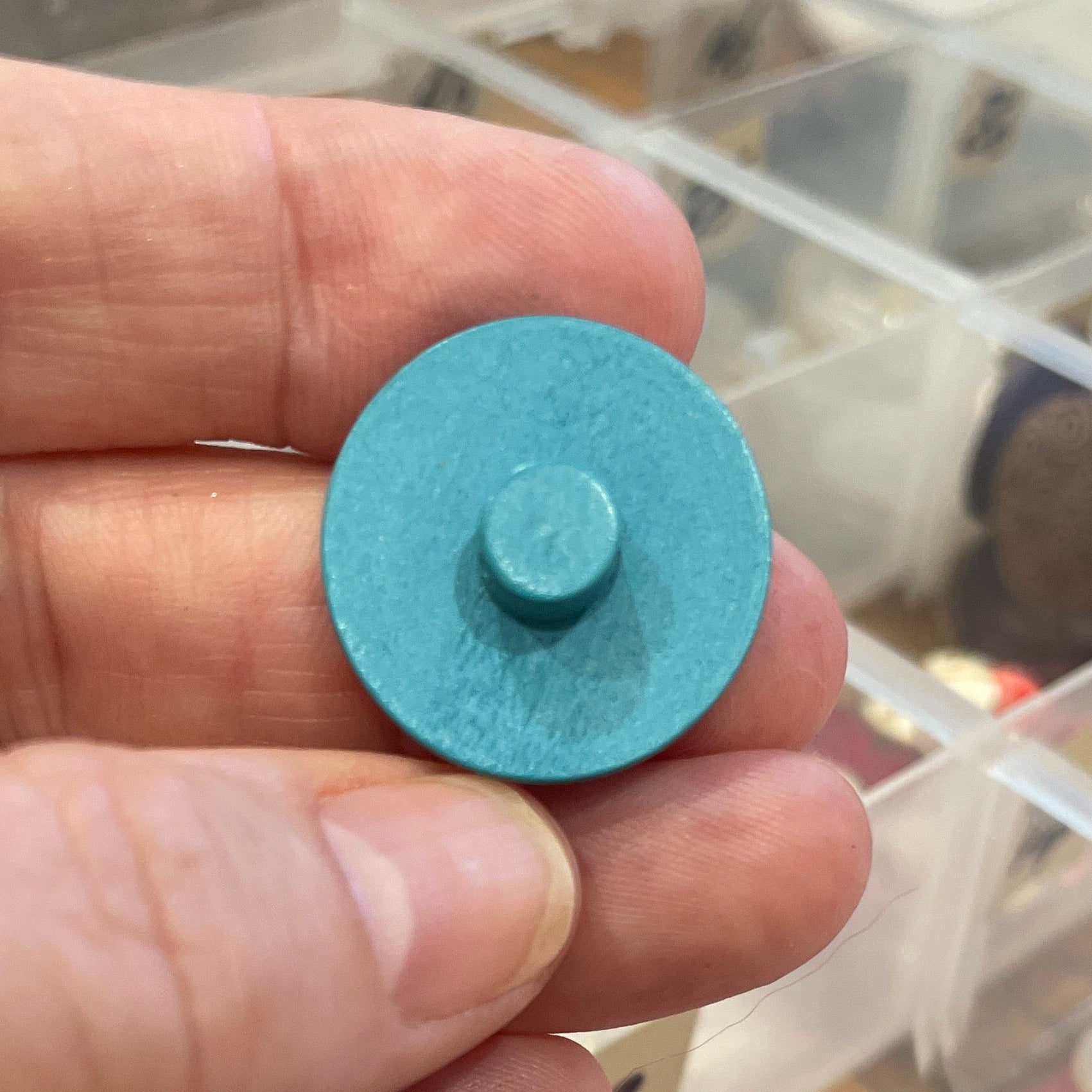 Hand holding a blue button with a container of buttons in the background