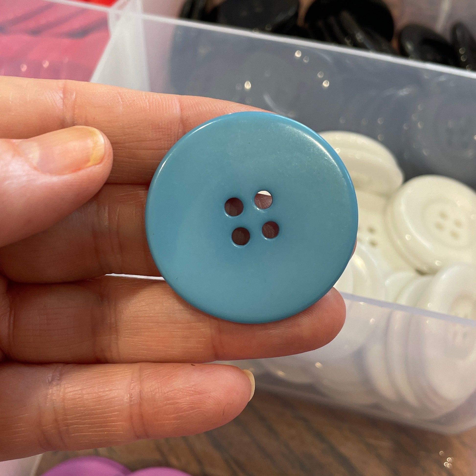 Hand holding a blue button with a container of buttons in the background