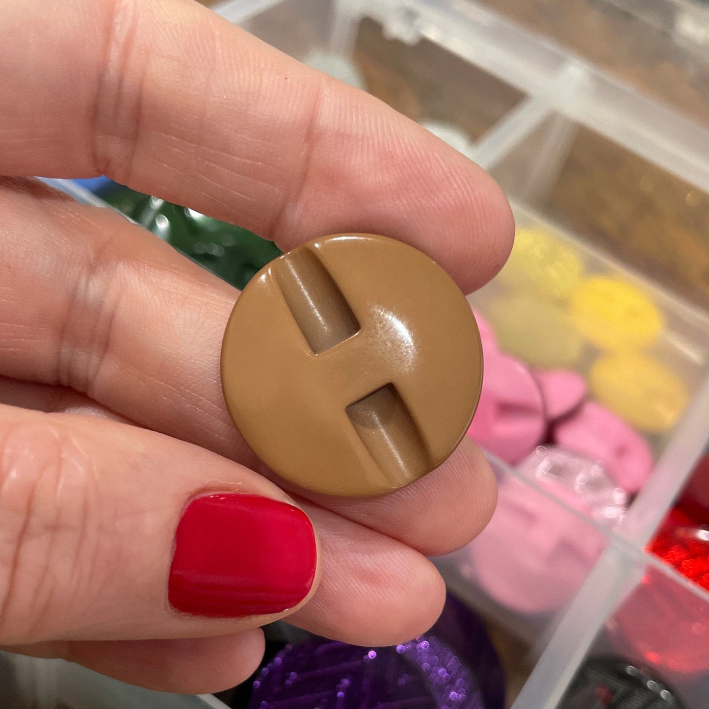 Hand holding a gold button with a colorful assortment of buttons in the background