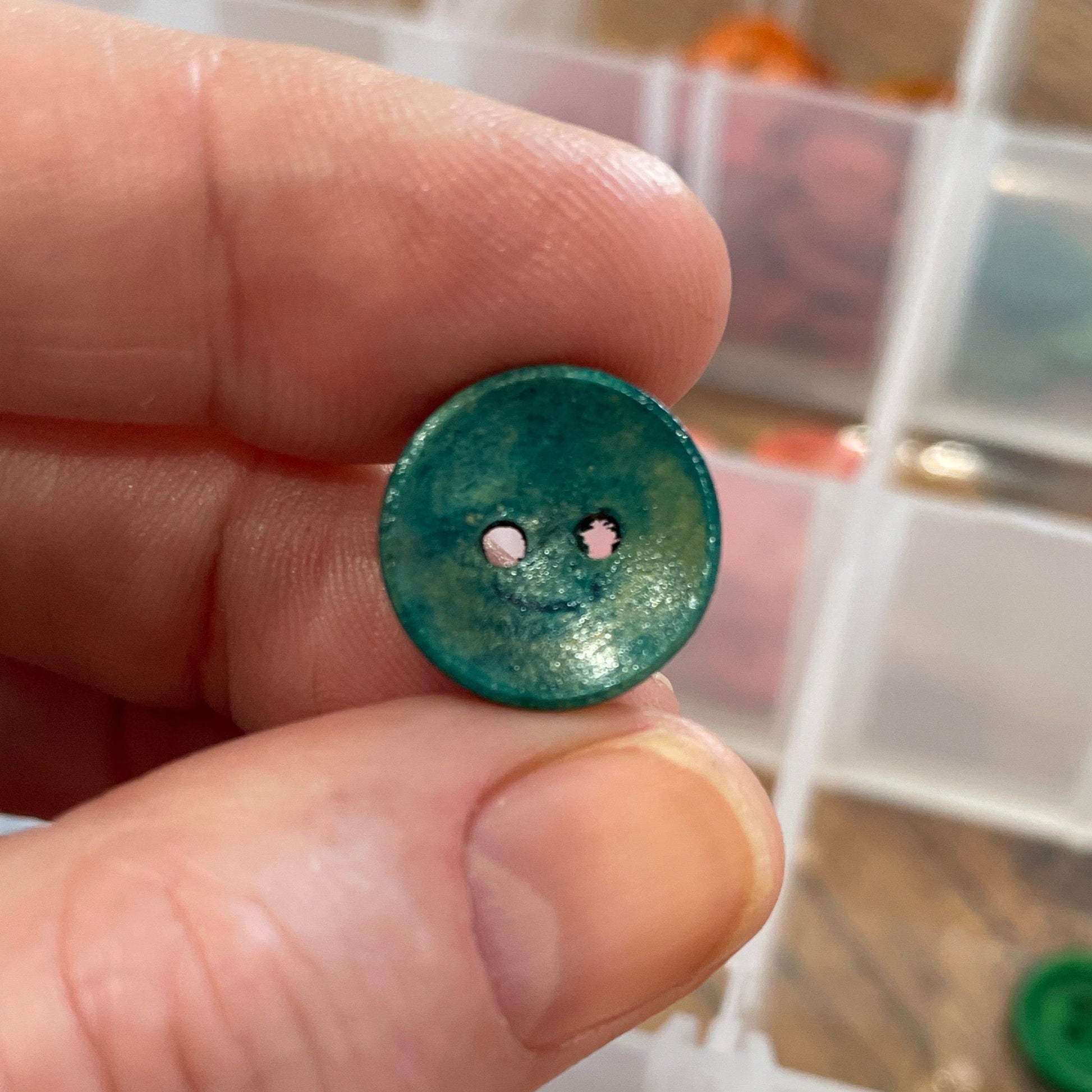 Hand holding a green button with a clear container of buttons in the background