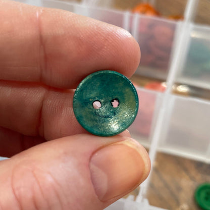 Hand holding a green button with a clear container of buttons in the background