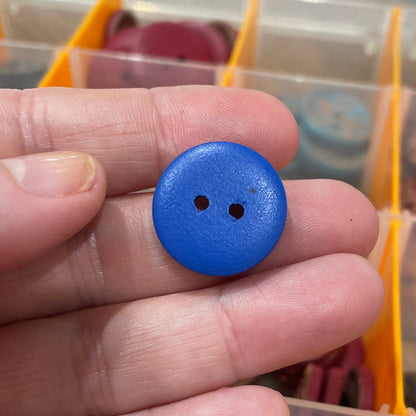 Hand holding a blue button with a blurred background of button collection
