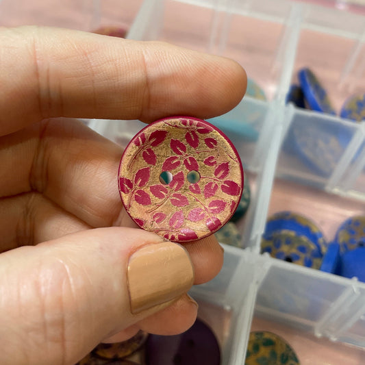 Hand holding a decorative button with a container of other buttons in the background