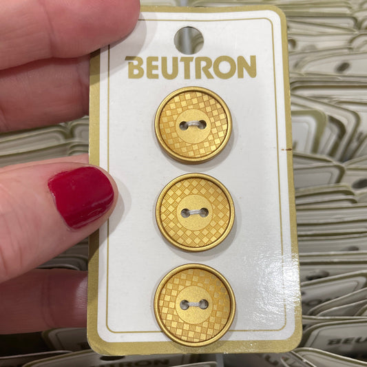Gold circular buttons on a BEUTRON card held by a hand with red nail polish.