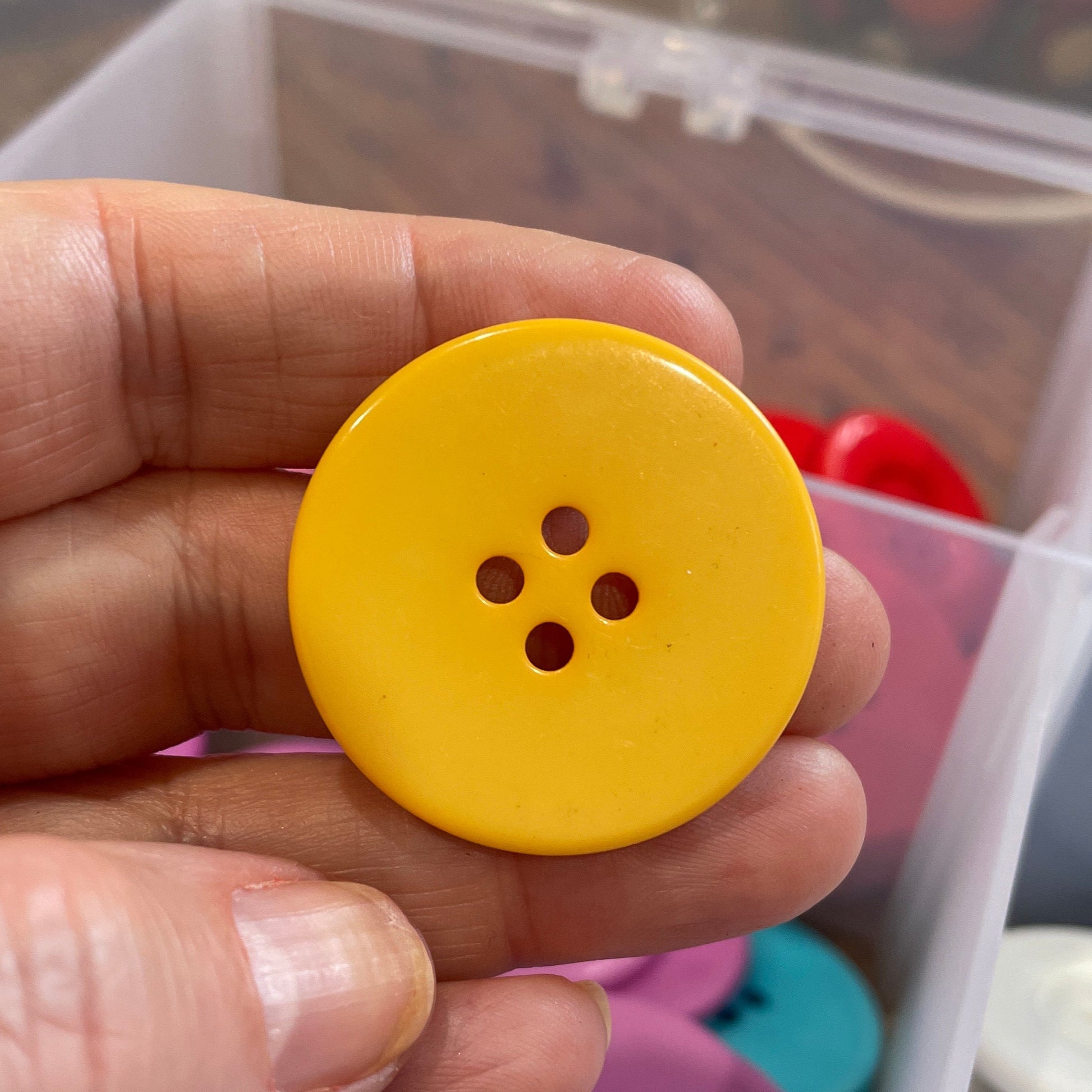 Yellow button held in a hand with a container of buttons in the background