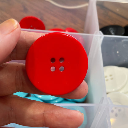 Hand holding a red button with a clear container of buttons in the background