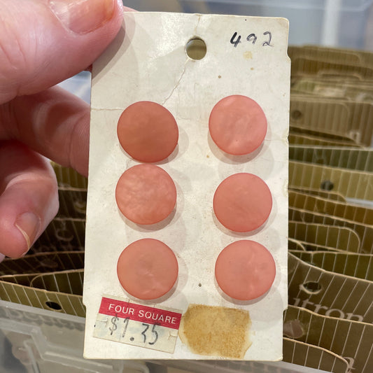 Buttons in a clear container on a wooden surface