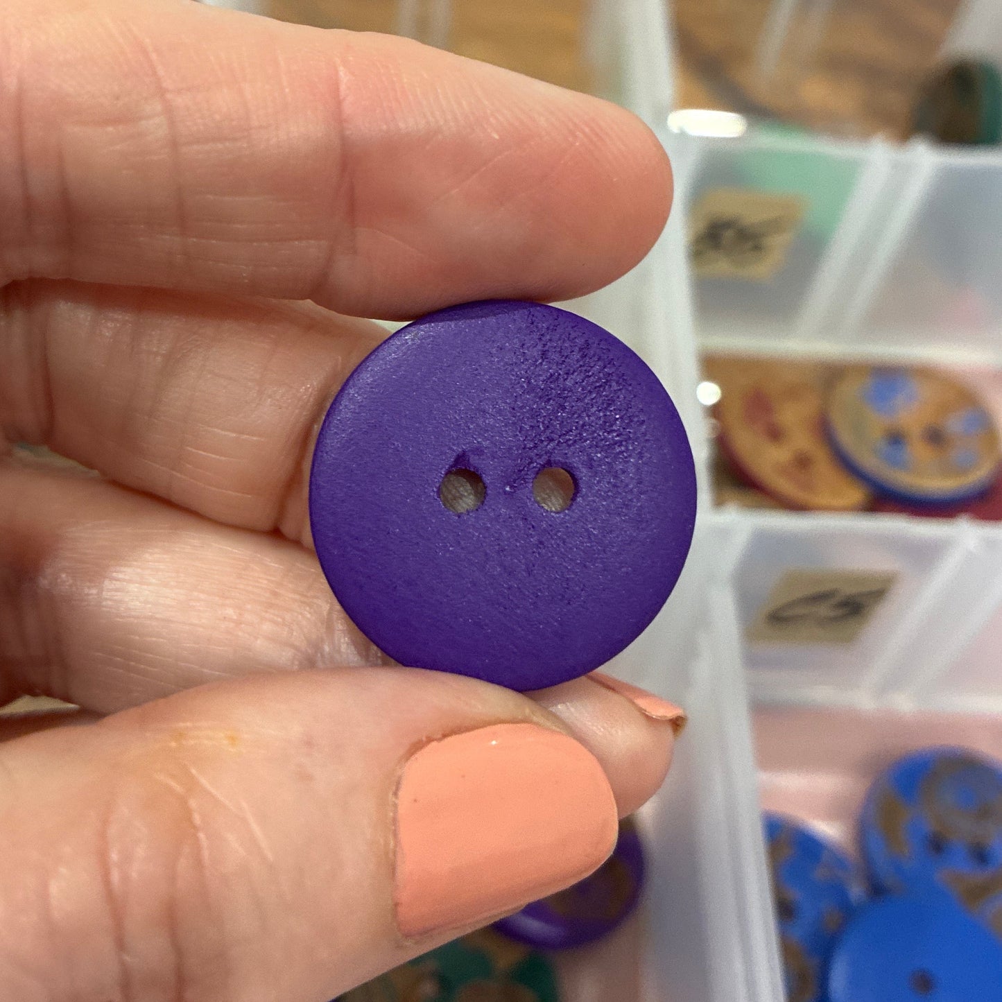 Hand holding a purple button with a container of buttons in the background