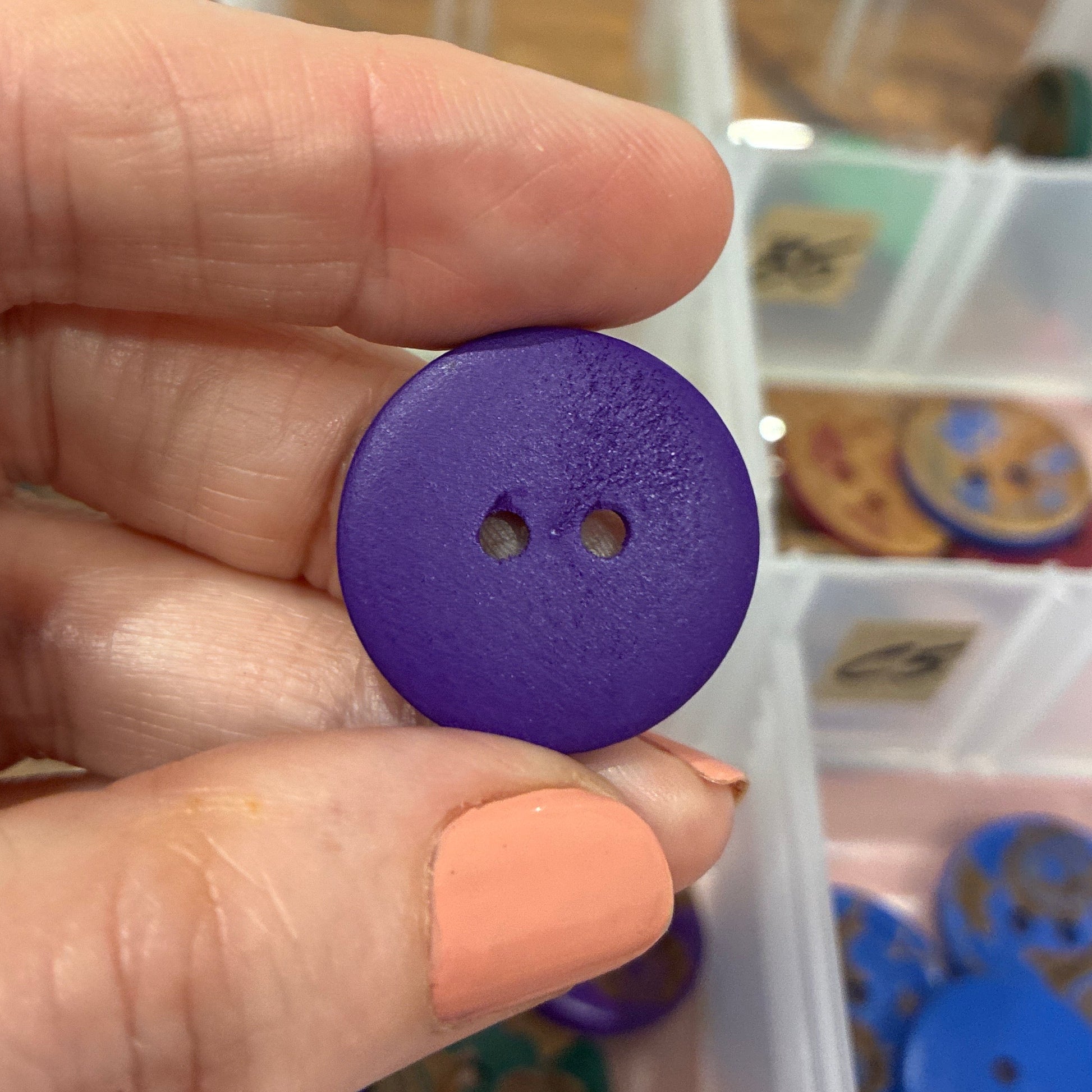 Hand holding a purple button with a container of buttons in the background