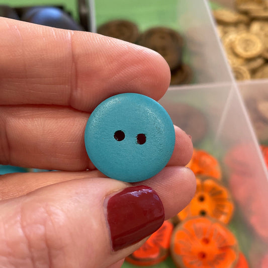 Hand holding a blue button with a container of colorful buttons in the background