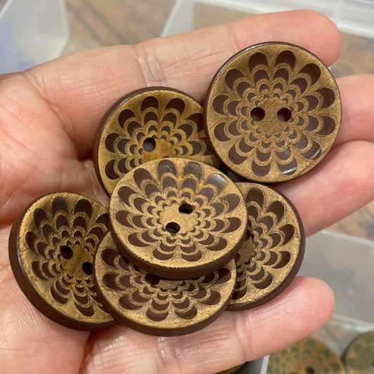Hand holding decorative wooden buttons with a clear container of more buttons in the background.