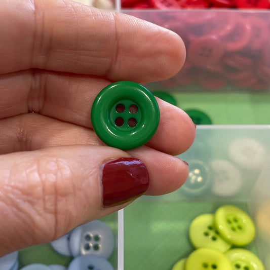 Hand holding a green button with a container of colorful buttons in the background