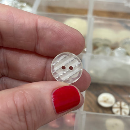 Hand holding a button with a background of button collection in a box