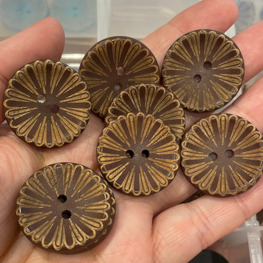 Hand holding six bronze floral-patterned buttons with a container of buttons in the background.