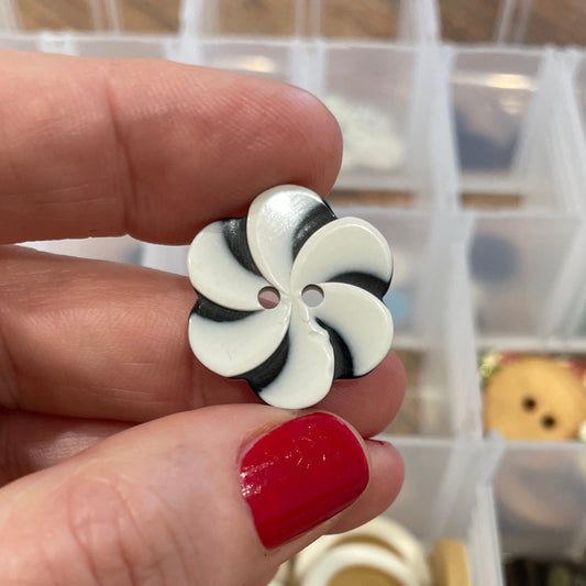 Hand holding a black and white flower-shaped button with a container of buttons in the background.