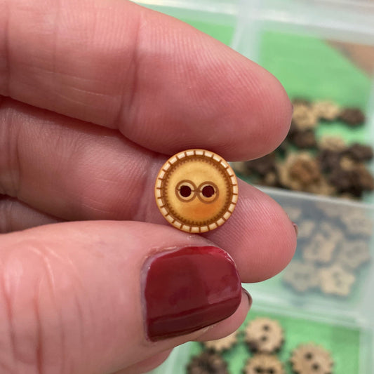 Gold button held by a hand with red nail polish, against a background of more buttons in a container.