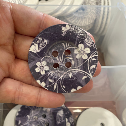 Hand holding a floral-patterned button with a container of buttons in the background