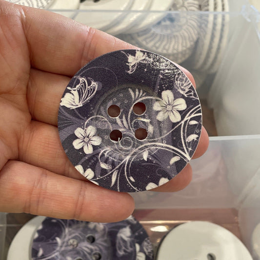 Hand holding a floral-patterned button with a container of buttons in the background