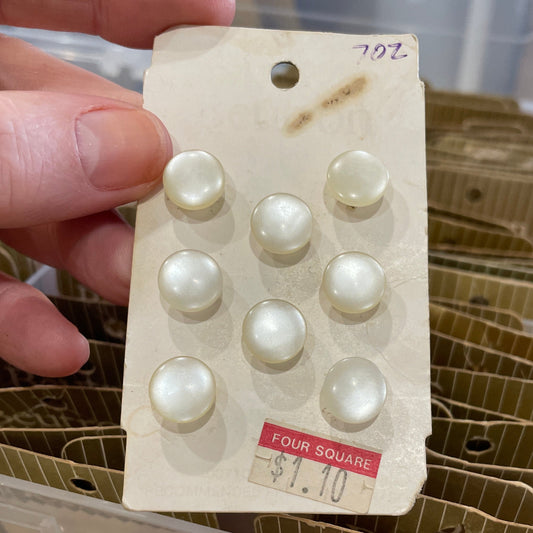 Card with buttons held by a hand, with a container of similar items in the background.
