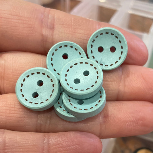 Hand holding light blue buttons with a container of assorted buttons in the background