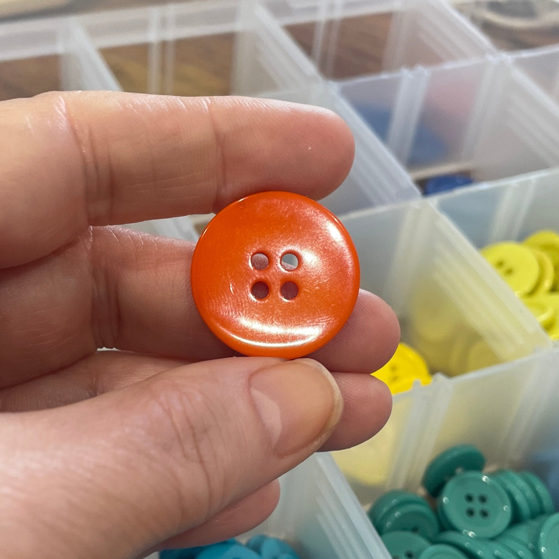 Hand holding an orange button with a background of colorful buttons in containers.