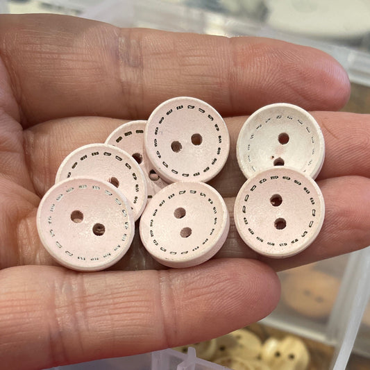 Hand holding beige buttons with a container of pink and orange buttons in the background