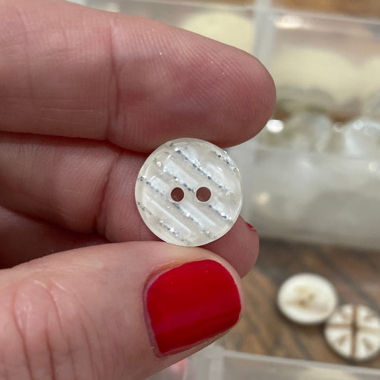 Hand holding a small white button with a clear container of buttons in the background