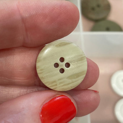 Hand holding a beige button with a blurred background of button collection