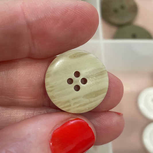 Hand holding a beige button with a blurred background of button collection