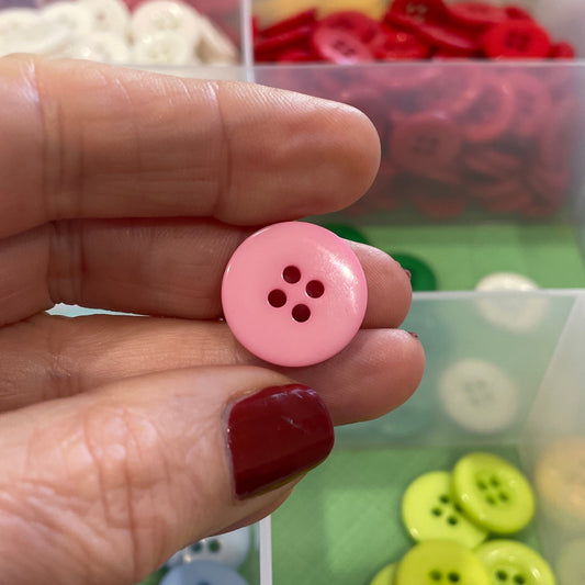Pink button held by a hand with a colorful button organizer in the background