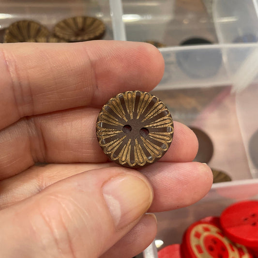 Hand holding a bronze button with a container of various buttons in the background