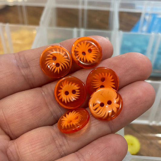 Hand holding small orange buttons with a blurred background of more buttons in containers.