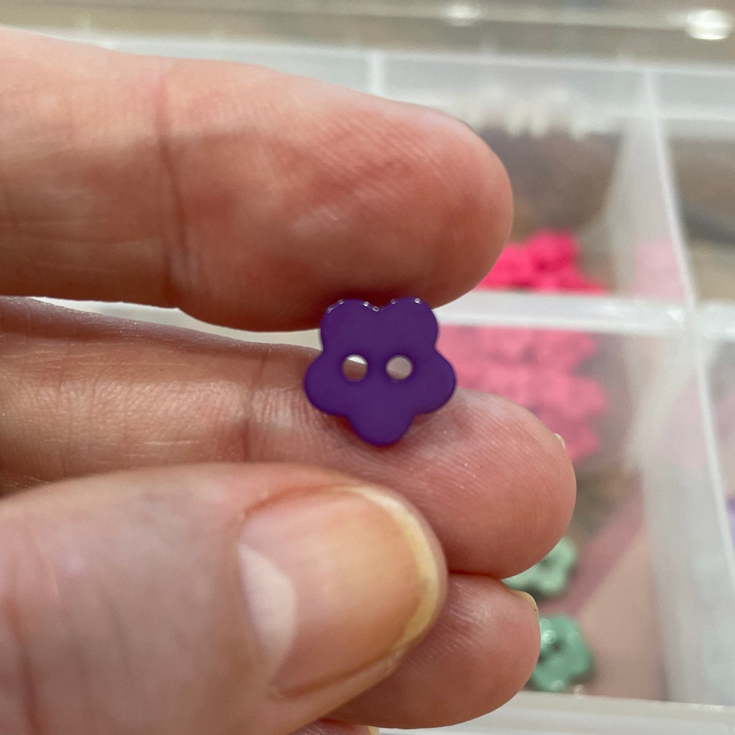 Hand holding a purple flower-shaped object with a container of colorful flowers in the background.