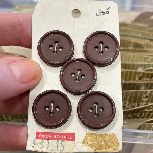 Card with five brown buttons held by a hand, with a blurred background