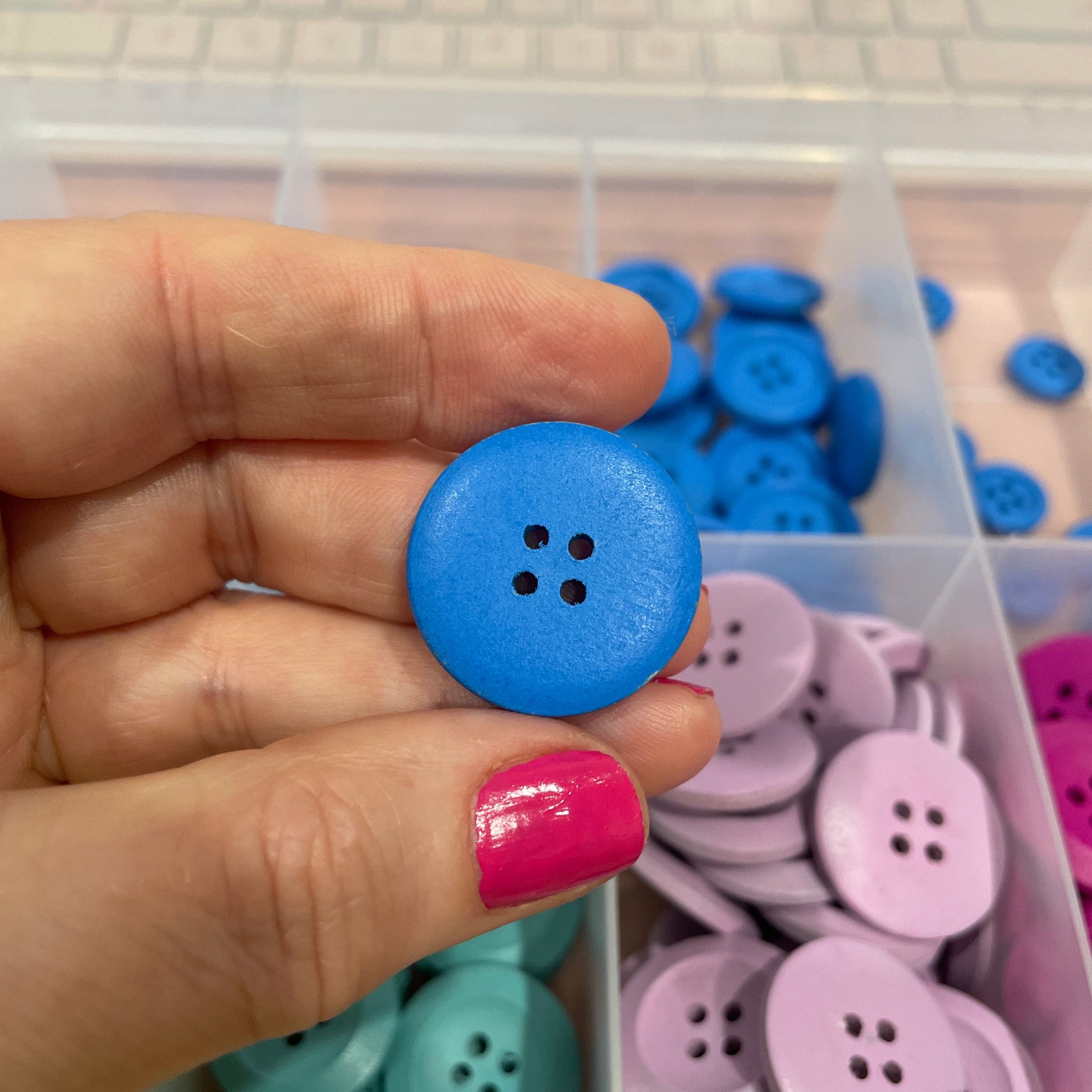 Hand holding a blue button with a container of colorful buttons in the background