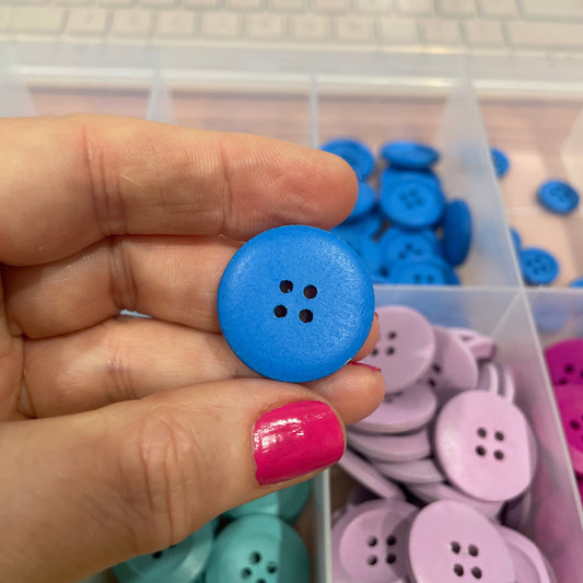 Hand holding a blue button with a container of colorful buttons in the background