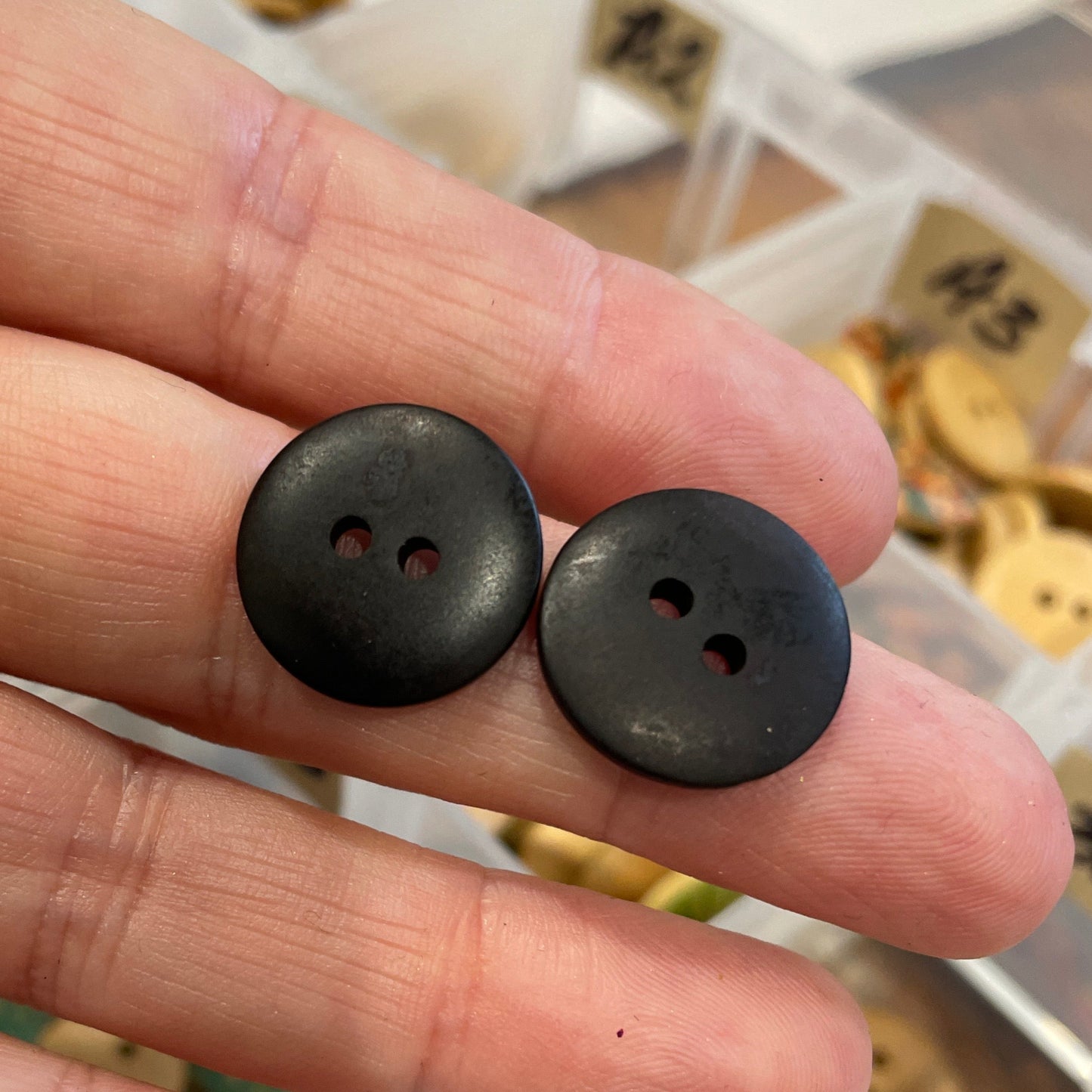 Black buttons held between fingers with a container of buttons in the background