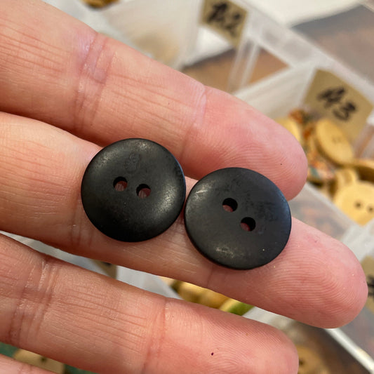 Black buttons held between fingers with a container of buttons in the background